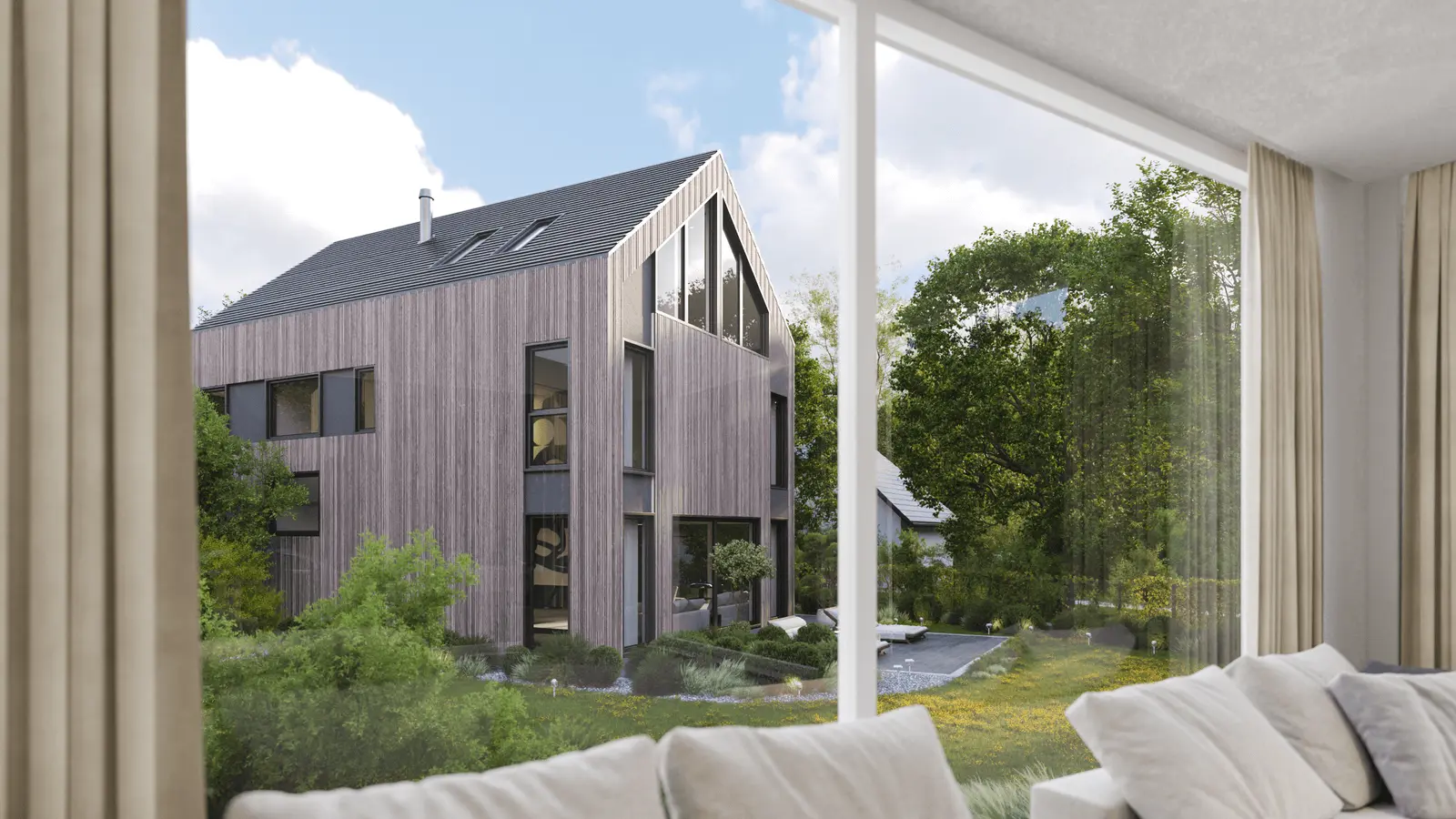 Der Blick aus einem Fenster zeigt ein modernes Holzhaus mit dreieckigem Dach, umgeben von grünen Bäumen und Sträuchern unter einem teilweise bewölkten Himmel.