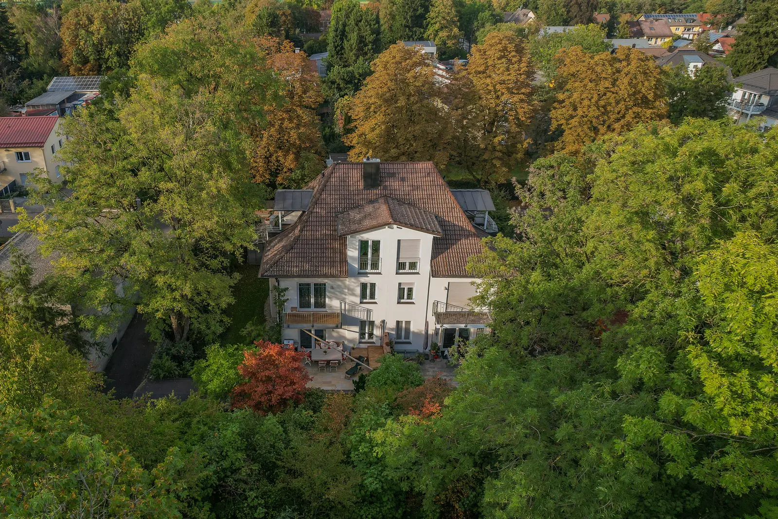 Eine Luftaufnahme eines mehrstöckigen Hauses mit braunem Ziegeldach, umgeben von altem Baumbestand in einem Wohnviertel.